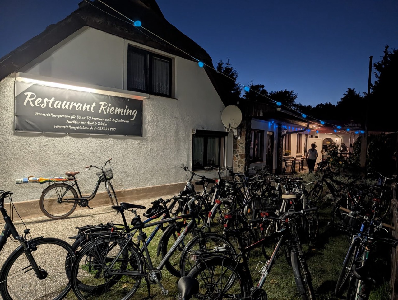 Restaurant Rieming unter dem Reetdach in der Dämmerung mit beleuchtetem Schild, Lichterkette und Fahrrädern